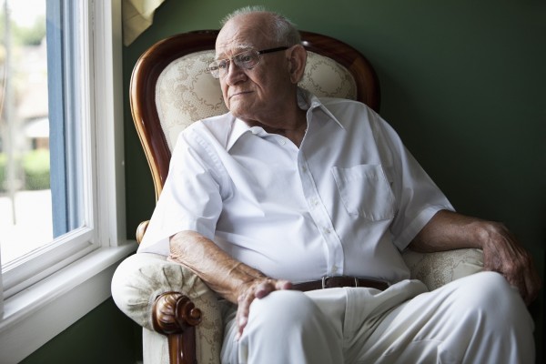 Contemplative senior man (80s) sitting in chair at home, looking out the window.