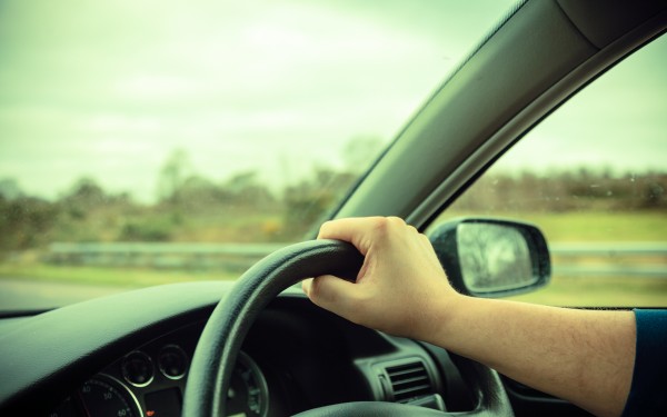 Male driver hands holding steering wheel of a car and road