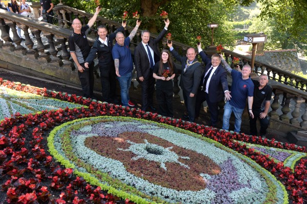 Photo caption:- All at the opening. Attending was the Lord Provost of Edinburgh and the Chief Executive Mark Bibby of Poppy Scotland. The finishing touches have been put to EdinburghÕs historic floral clock, which this summer has been designed to mark 100 years since the signing of the Armistice, leading to the end of the First World War. The West Princes Street Gardens landmark, maintained by the City of Edinburgh Council, has been created in partnership with Armed Forces charity Poppyscotland as part of their year-long fundraising campaign, The 1918 Poppy Pledge. On Tuesday (3 July), EdinburghÕs Lord Provost, Councillor Frank Ross, was joined by PoppyscotlandÕs Chief Executive Mark Bibbey, workers and ex-servicemen from PoppyscotlandÕs Lady Haig Poppy Factory, where all of the countryÕs five million poppies are made each year, and parks staff responsible for creating the clock. Together they officially unveiled the design, which features a poppy flanked by two First World War soldiers. PoppyscotlandÕs 1918 Poppy Pledge aims to commemorate those who fell in the First World War, with funds raised helping to provide support to those in the Armed Forces community. The Lord Provost, Councillor Frank Ross, said: ÒIt is an honour to be able to support the life-changing work carried out by Poppyscotland with this floral clock design, which this year will provide a particularly poignant reminder of the signing of the Armistice, 100 years on from the end of World War One. ÒAs always, I am delighted to officially unveil this striking and much-loved creation, which is a source of enjoyment and fascination for so many people every day, and IÕd like to congratulate our dedicated parks staff, whose hard work has paid off once again.Ó Gordon Michie, Head of Fundraising at Poppyscotland, said: ÒI am delighted that The City of Edinburgh Council has chosen to commemorate the signing of the Armistice this year by dedicating the world-famous Floral Clock to Poppyscotland and our work supporting beneficiaries across Scotland. ÒThis support, which is part of our wider #1918PoppyPledge campaign, will give a unique, powerful and emotive view of Remembrance in the vibrancy and colour of the 35,000 flowers that have been planted. It will be a place to not only visit and take photographs, but also a place to reflect on the sacrifices that so many gave on our behalf. Furthermore, it is fitting that the floral clock is situated close to so many other monuments in West Princes Street Gardens to those that have served.Ó The floral clock was first created in 1903 by the Edinburgh Parks Superintendent, John McHattie. The clock initially operated with only an hour hand with a minute hand added in 1904, followed by an accompanying cuckoo clock in 1952. Until 1972 the clock was operated mechanically, and had to be wound daily. Since 1946 it has been designed in honour of various organisations and individuals, including the Girl Guides Association, Robert Louis Stevenson and the Queen, for her Golden Jubilee. It has taken two gardeners more than a month to plant the 35,000 flowers and plants used to create the clock, which will be in bloom until October. Poppyscotland provides life-changing support to the Armed Forces community, with money raised from the Scottish Poppy Appeal and year-round fundraising enabling the charity to provide tailored funding and assistance, as well as advice, employment, housing, healthcare and respite. Find out more about EdinburghÕs parks and green spaces online. Floral clock fact file The clock was created in 1903 May Ð when planting begins 35,000 plants are used in the design (compared to 13,000 in 1930s; 25,000 50s-60s) 1952 Ð when the cuckoo was added In 1946 the clock began celebrating a different event or anniversary Clock circumference: 36 ft Clock width: 11 ft 10 ins 80lbs Ð weight of large hand 50lbs Ð weight of small hand 1973 Ð when the clock began being operated electrically EdinburghÕs is believed to be oldest floral clock in the world